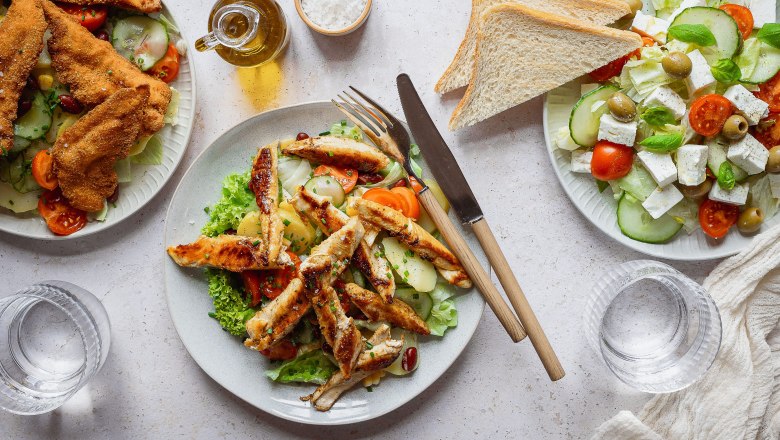 Drei Teller mit verschiedenen Salaten und Brot auf einem Tisch.