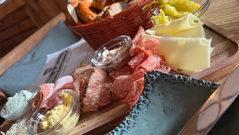 Eine rustikale Jause mit Wurst, K&auml;se, Brot und Aufstrichen auf einem Holzteller.