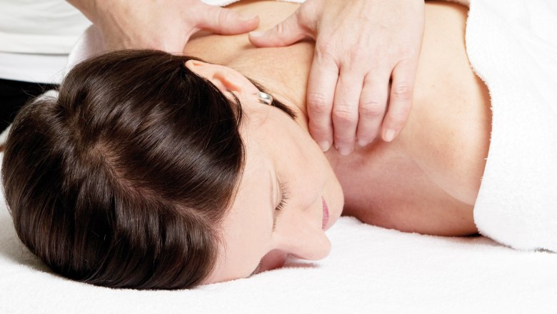 Eine Frau erhält eine Nackenmassage auf einem weißen Handtuch liegend.