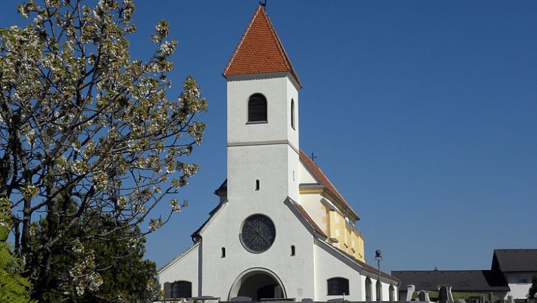 St. Anna Kirche in Wiesmath mit blauem Himmel und bl&uuml;hendem Baum im Vordergrund.