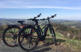 Zwei E-Bikes stehen auf einem Hügel mit Blick auf eine hügelige Landschaft.