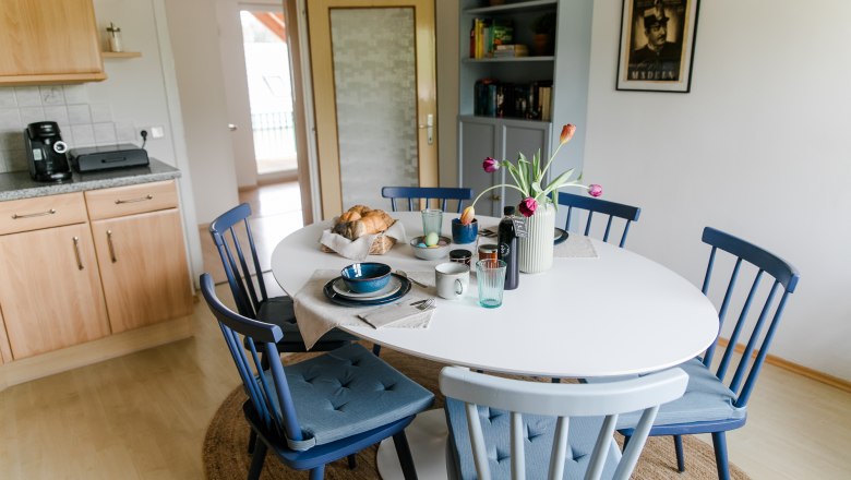Essbereich in einer Küche mit rundem Tisch, blauen Stühlen und gedecktem Frühstückstisch.