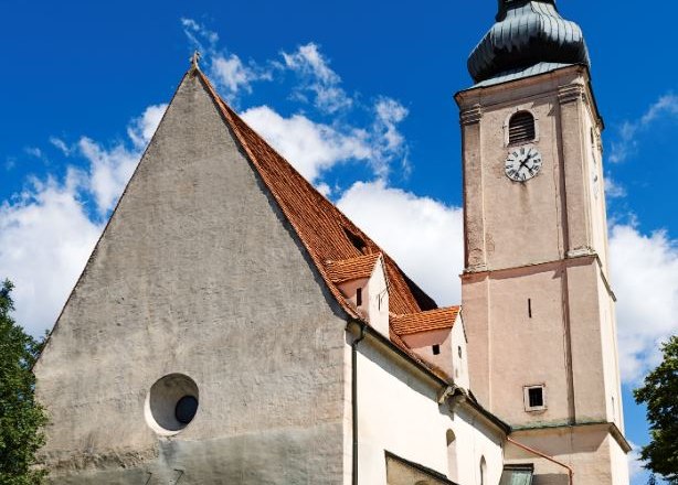 Pfarrkirche Wiesmath mit Turm, Friedhofsmauer aus Stein und Uhr vor blauem Himmel.