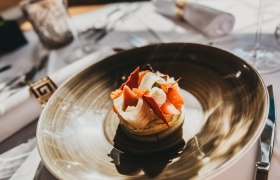 Ein kunstvoll angerichtetes Gericht auf einem braunen Teller in einem Restaurant.