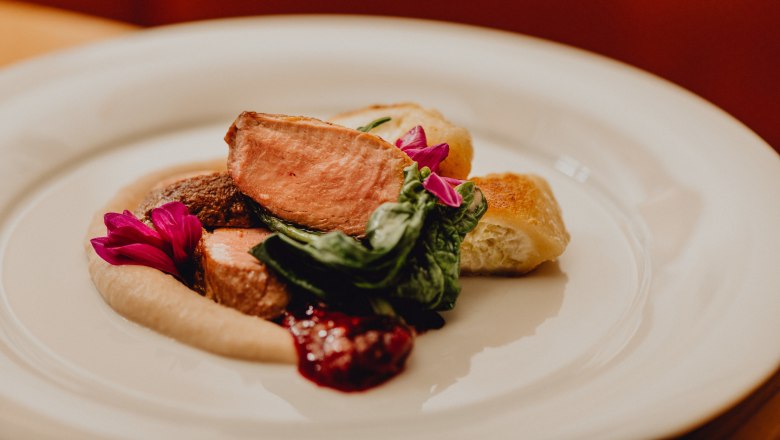 A plate of pink roast duck, cream tartlets, chestnut pur&eacute;e and green leaves, garnished with edible flowers.