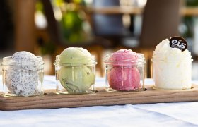 Vier Gläser mit verschiedenen Eissorten auf einem Holzbrett.