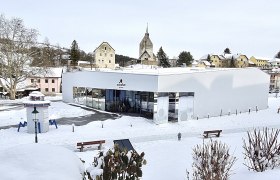 Modern building in the snow with a church in the background.