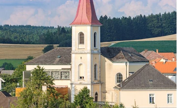 Pfarrkirche Hochwolkersdorf mit rotem, spitzen Turmdach und umliegender Landschaft.