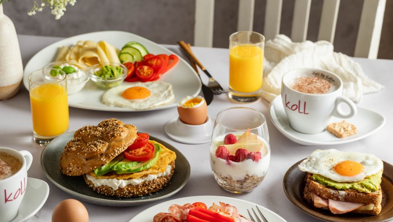Fr&uuml;hst&uuml;ckstisch mit Br&ouml;tchen, Aufschnitt, Spiegelei, Joghurt mit Beeren, Orangensaft und Kaffee.