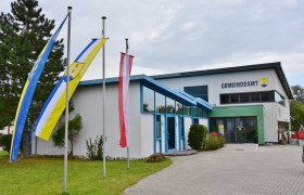 Ein modernes Gebäude mit der Aufschrift 'Gemeindeamt' und drei Fahnenmasten davor.