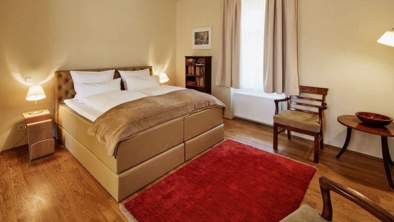 Ein gemütliches Schlafzimmer mit einem großen Bett, zwei Nachttischen mit Lampen, einem roten Teppich und Holzmöbeln.