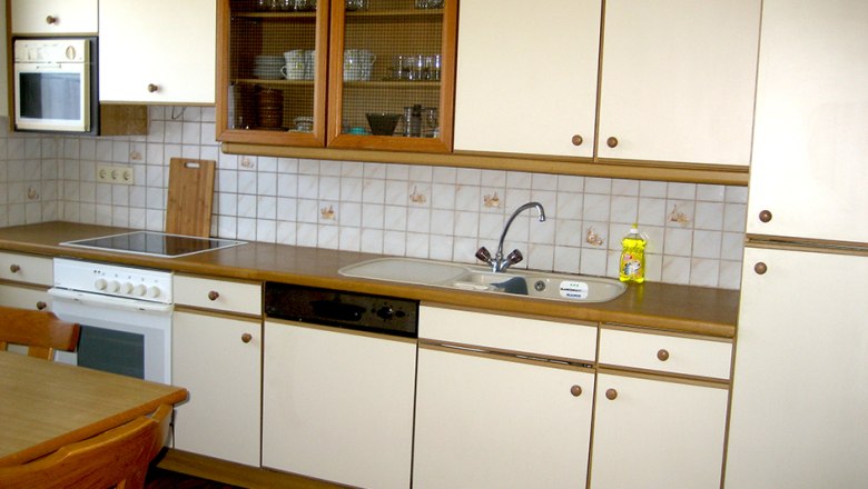 Kitchenette with white cupboards, stove, sink and dishwasher.