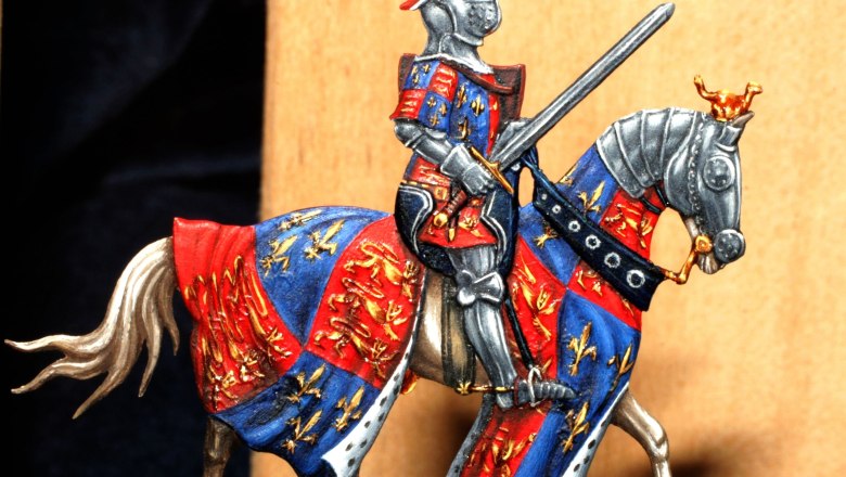 Zinnfigur eines Ritters in Rüstung auf einem Pferd mit buntem Wappenrock.