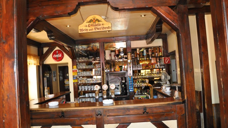 Innenansicht einer rustikalen Bar mit Holzbalken und einer gut best&uuml;ckten Theke.