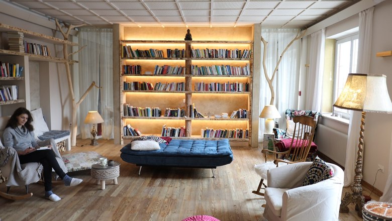 Gemütliche Bibliothek mit großen, beleuchteten Bücherregal, Sesseln und einer Person, die liest.