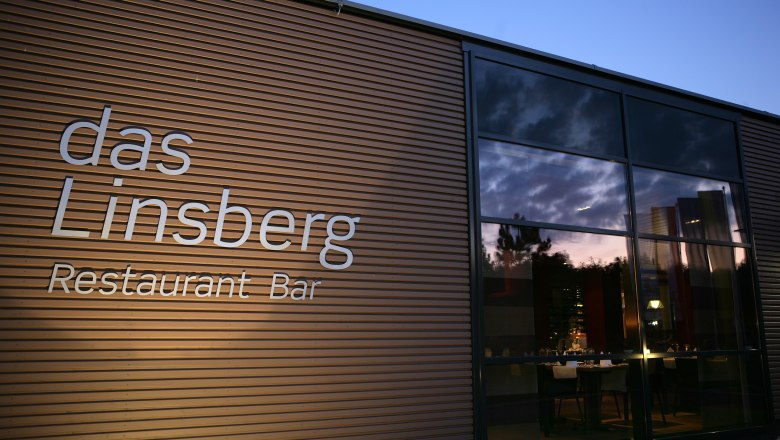 Außenansicht des Restaurants 'das Linsberg' bei Dämmerung mit beleuchtetem Innenraum.