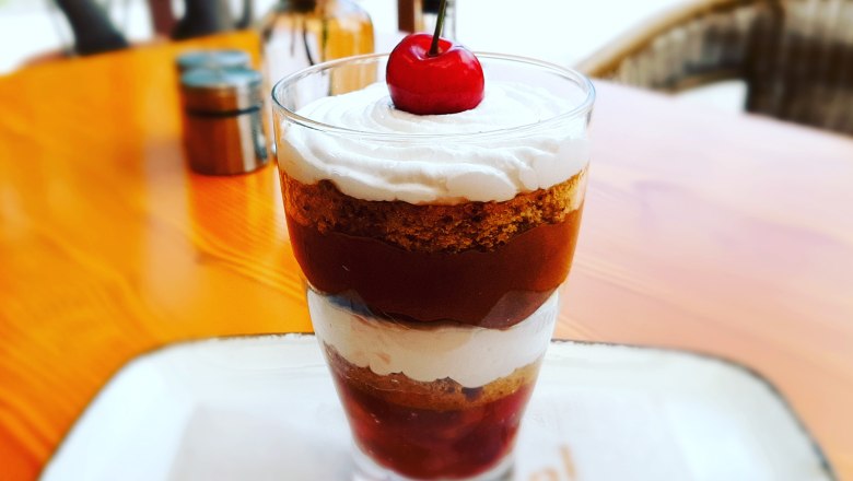 Ein Dessert im Glas mit Schichten aus Sahne, Kuchen und Kirschen, garniert mit einer Kirsche.