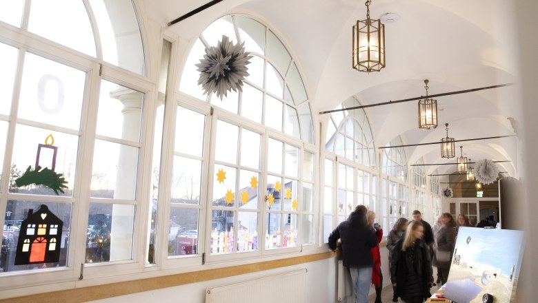 Ein heller Korridor im Schloss mit gro&szlig;en Fenstern und einem Stand am Christkindlmarkt mit Kunst.