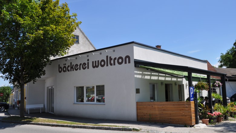 Au&szlig;enansicht der B&auml;ckerei Woltron mit Pflanzen und Parkpl&auml;tzen.