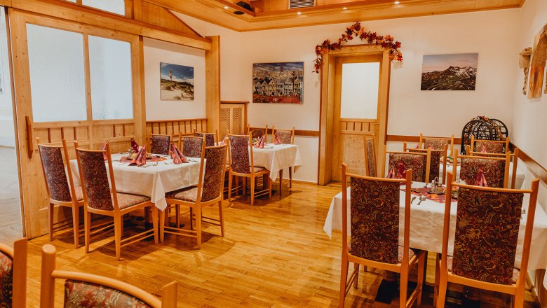 Gemütliche Gaststube mit Holzmöbeln und dekorierten Tischen, umgeben von Bildern an den Wänden.