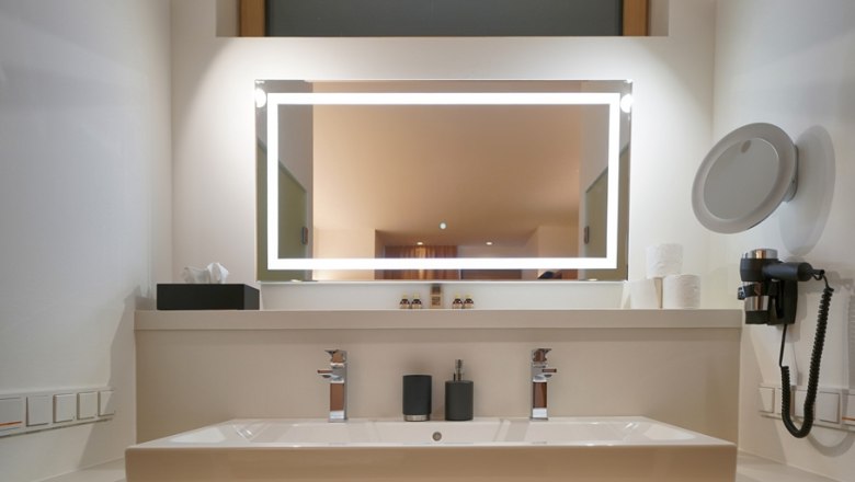 Modern washbasin with illuminated mirror, two taps, soap dispenser and hairdryer.