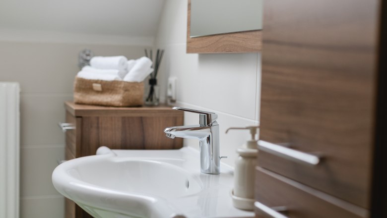 Modernes Badezimmer mit Waschbecken, Holzschr&auml;nken und Handt&uuml;chern in einem Korb.