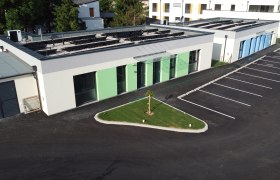 Au&szlig;enansicht von modernen Ferienbungalows mit gr&uuml;nem und blauem Anstrich, Parkplatz und kleinem Rasenbereich.