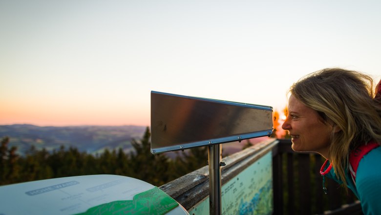 Frau schaut durch ein Fernrohr bei Sonnenuntergang auf einem Aussichtspunkt.