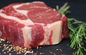 Ein rohes Steak auf einer dunklen Platte mit Gewürzen und Kräutern dekoriert.