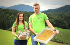 Zwei Personen in grünen T-Shirts präsentieren Nudeln vor einer Berglandschaft.