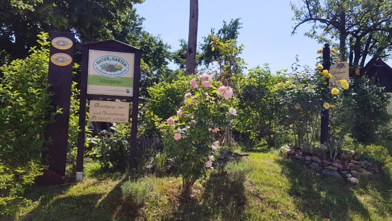 Eingang zu einem Schaugarten mit Schildern und bl&uuml;henden Rosen.
