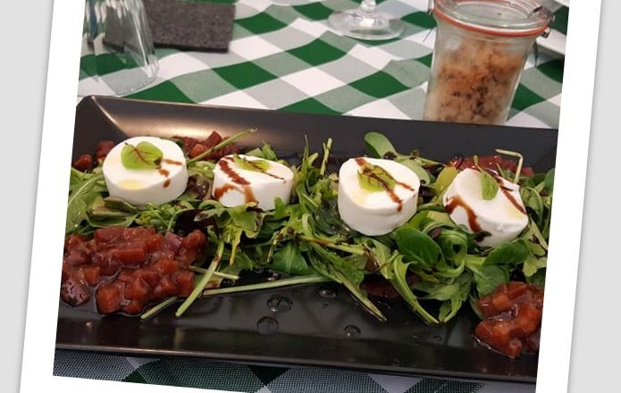 A plate of salad, mozzarella and tomatoes on a table with a green and white checkered tablecloth.