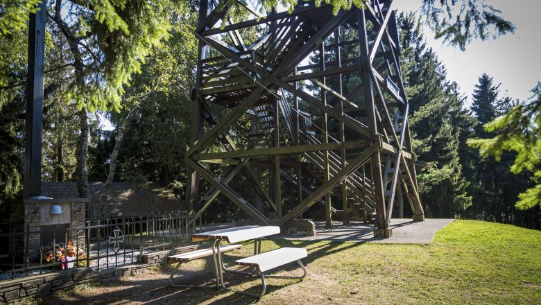 Holzaussichtsturm mit Picknicktisch im Vordergrund, umgeben von Bäumen.