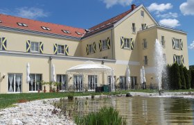 Großes gelbes Gebäude mit roten Dachziegeln, Springbrunnen und Pavillon im Vordergrund.
