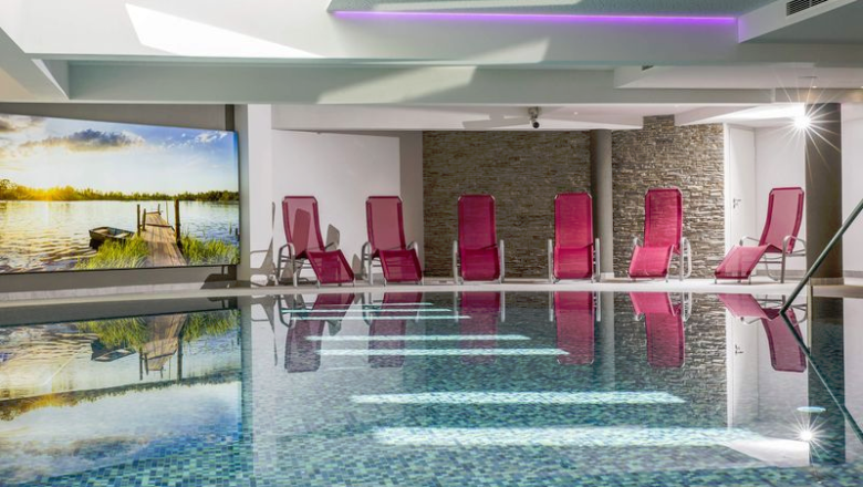 Hallenbad mit roten Liegest&uuml;hlen, Steinw&auml;nden und einem gro&szlig;en Wandbild.