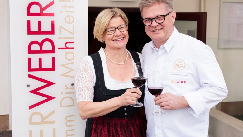 A man and a woman clink glasses of wine next to a sign that reads 'The Weaver'.