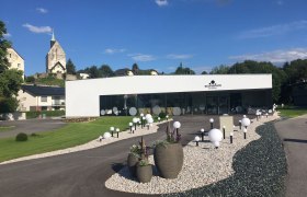 Modernes Gebäude des Sconariums mit Garten und Kirche im Hintergrund.