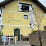 Gelbes Gebäude mit der Aufschrift 'Zum Stickelberg Wirtshaus', Terrasse mit bunten Stühlen und Sonnenschirm.