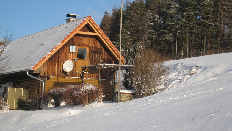 Wachahof in winter, © Wachahof A snow-covered wooden house on the edge of the forest with a blue sky.