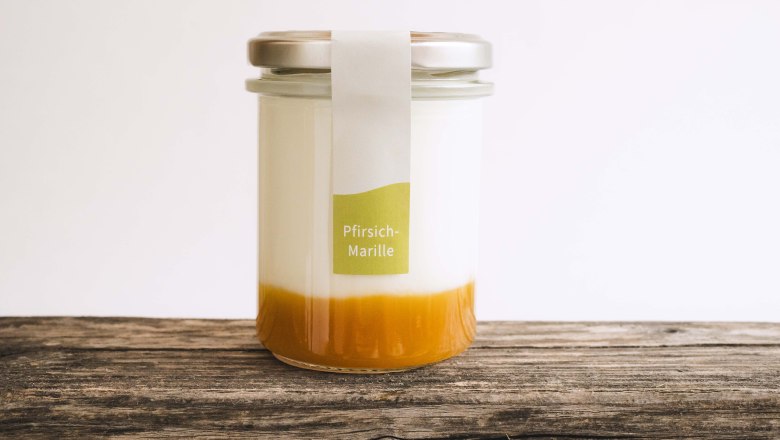 Ein Glas gef&uuml;llt mit Naturjoghurt und Fruchtspiegel auf einem Holztisch.