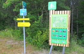 Wegweiser und Informationstafel f&uuml;r Radfahrer in Bad Erlach, umgeben von B&auml;umen.