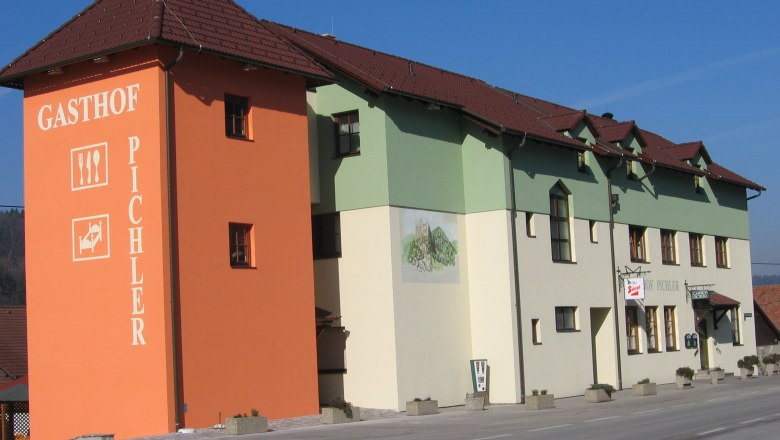 Ein Gasthof mit orangefarbenem Turm und grün-weißer Fassade an einer Straße.