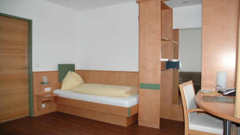 Ein einfach eingerichtetes Hotelzimmer mit Einzelbett, Schreibtisch und Holzverkleidung.