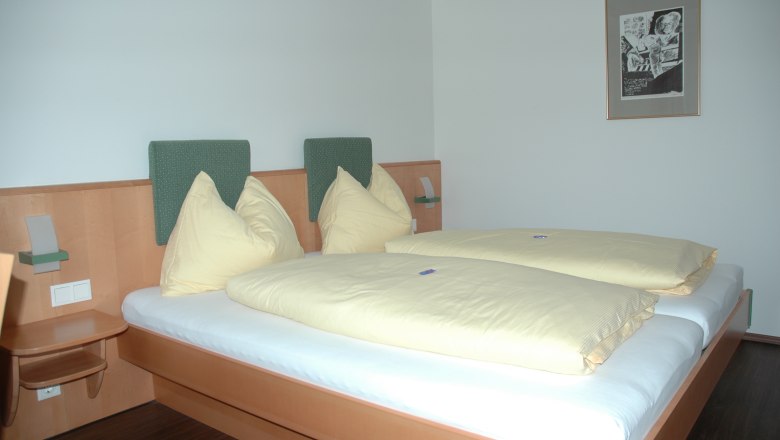 Hotelzimmer mit Doppelbett, gelber Bettwäsche und Wandbild.